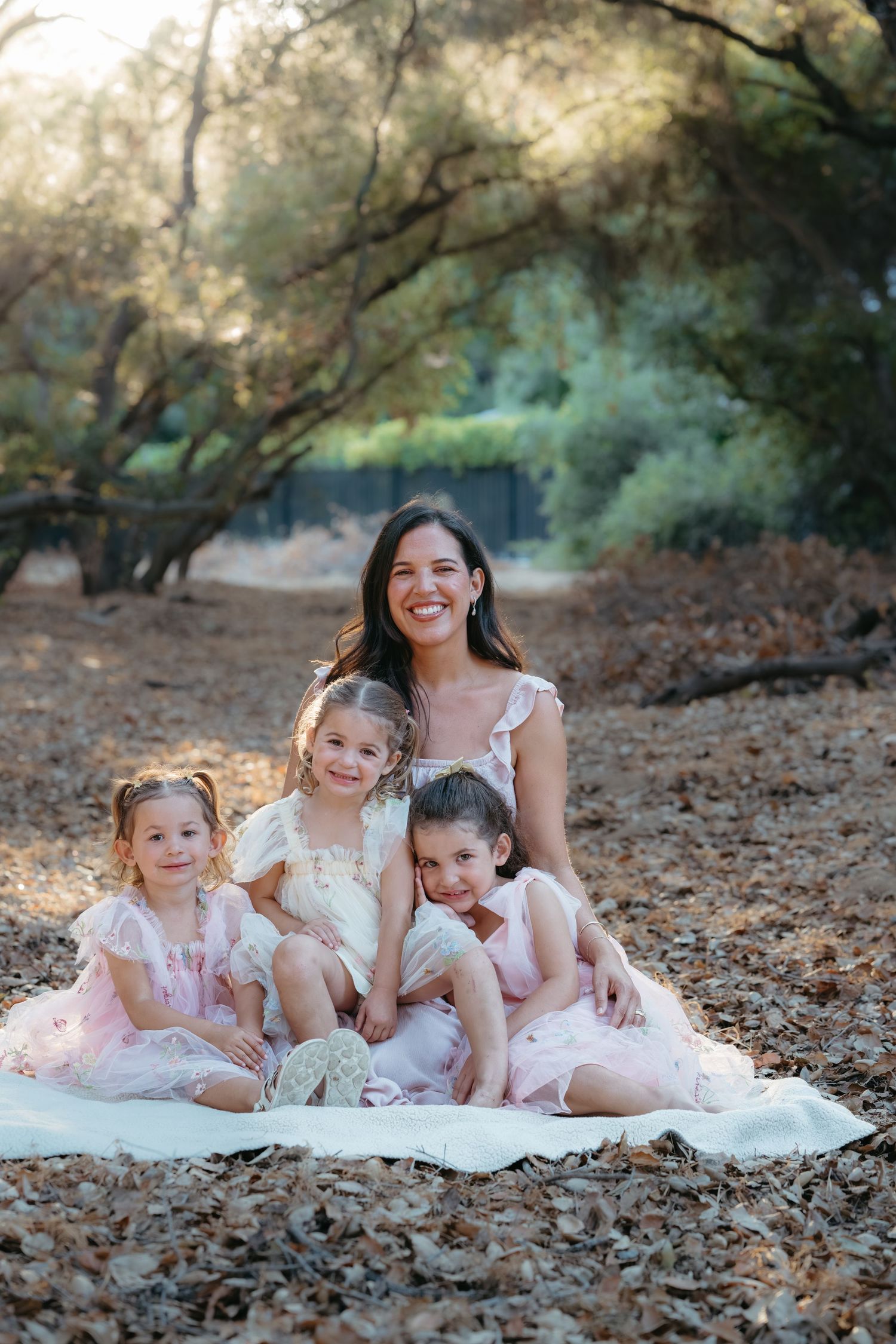 Family in matching pink and white dresses lying together on autumn leaves during outdoor photoshoot.