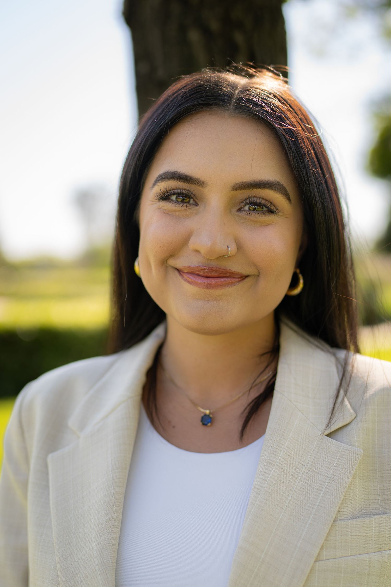 Professional headshots of person in cream blazer and white top against outdoor garden setting.