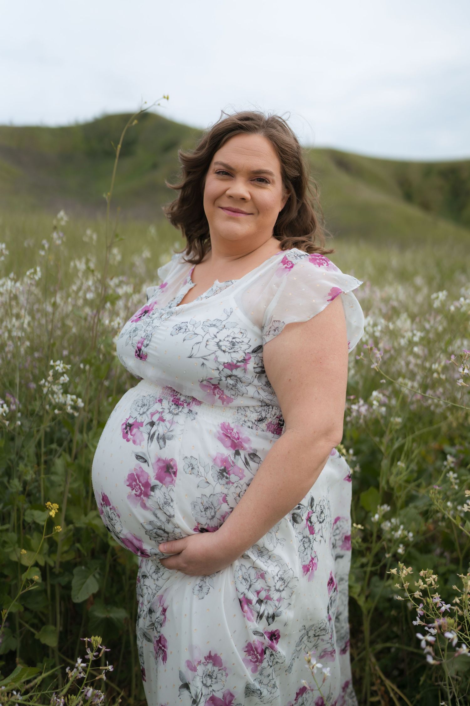 A person in a white floral dress stands in a meadow of wildflowers during a summer photo session.