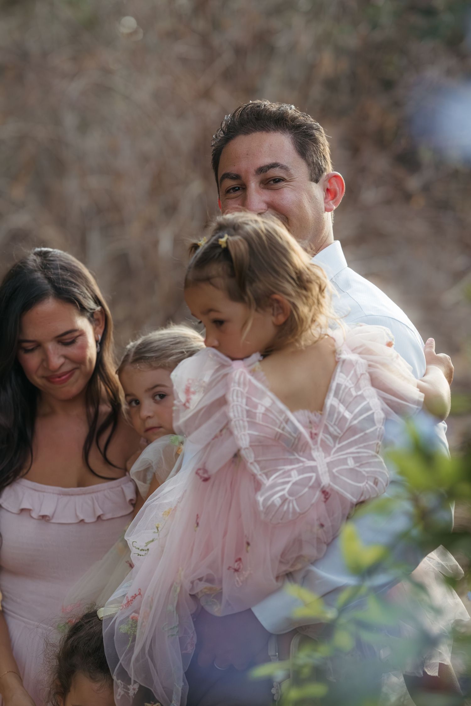 Intimate family moment captured through foliage during outdoor photo session.