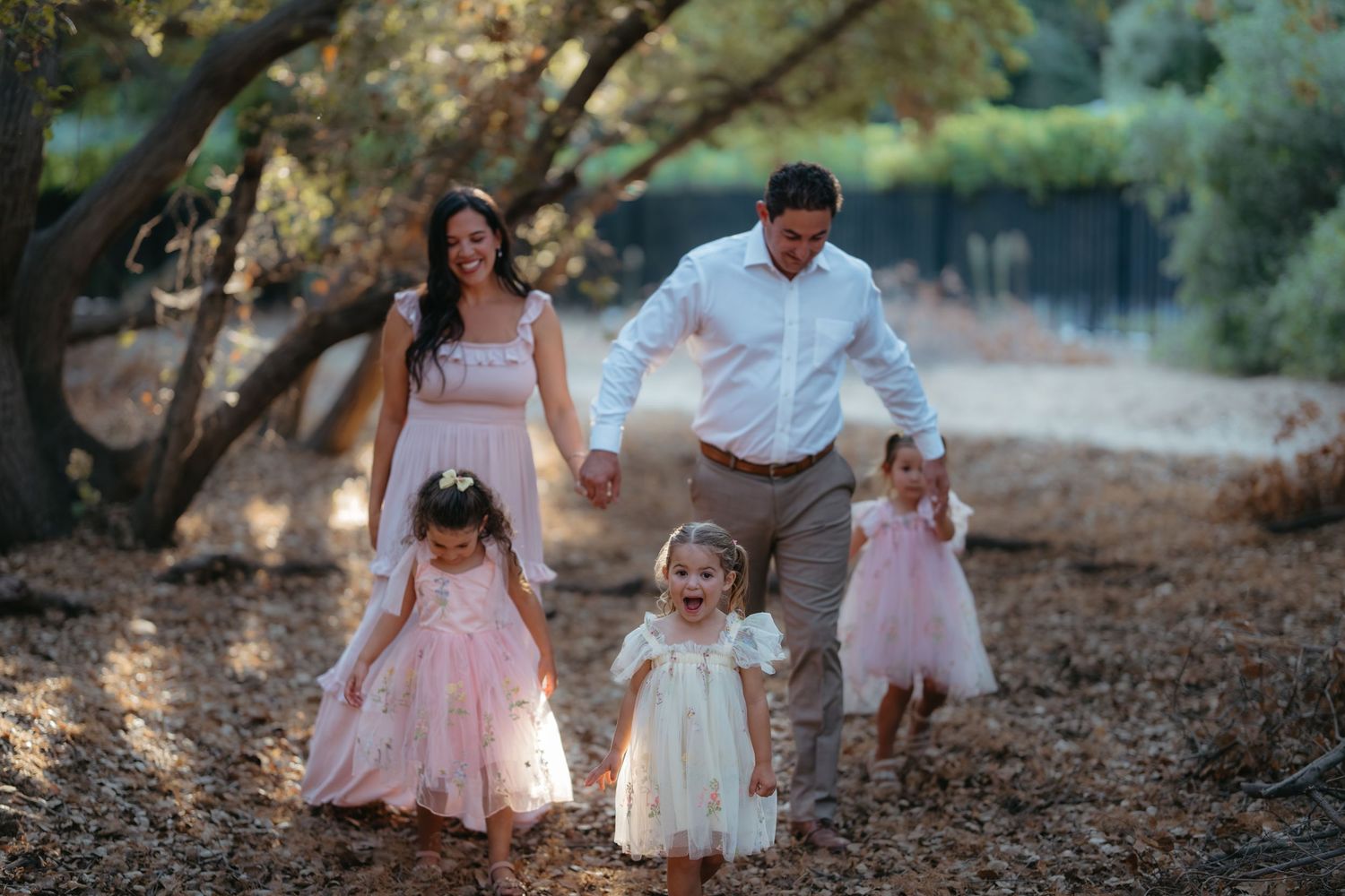 Family walks together through scenic wooded area at sunset wearing coordinated outfits.