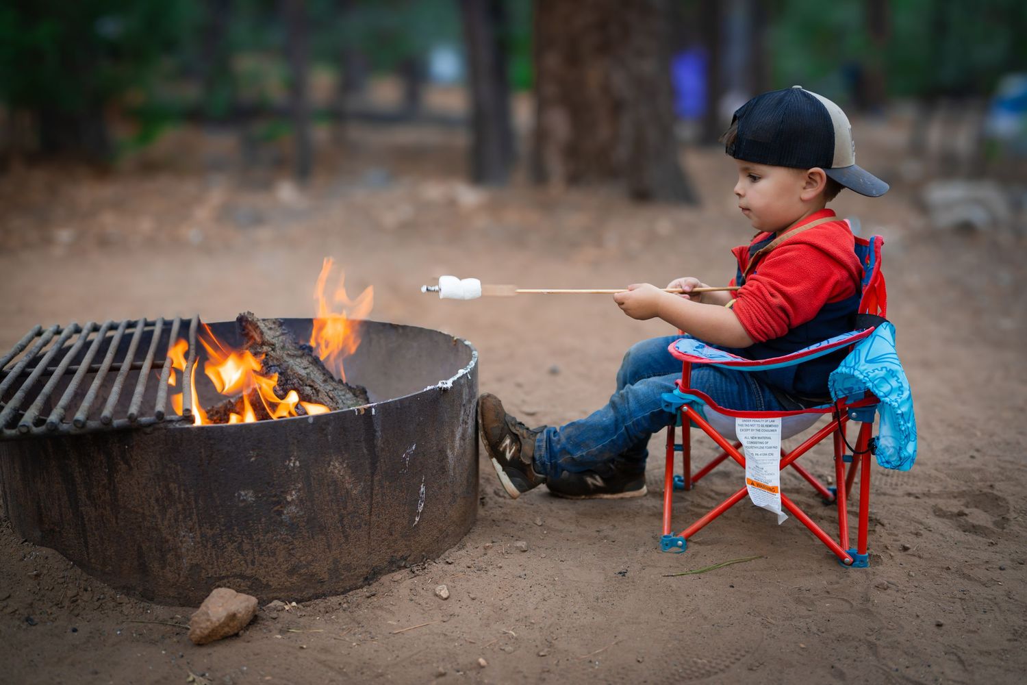 Small figure roasting marshmallow over campfire while sitting in red camping chair.