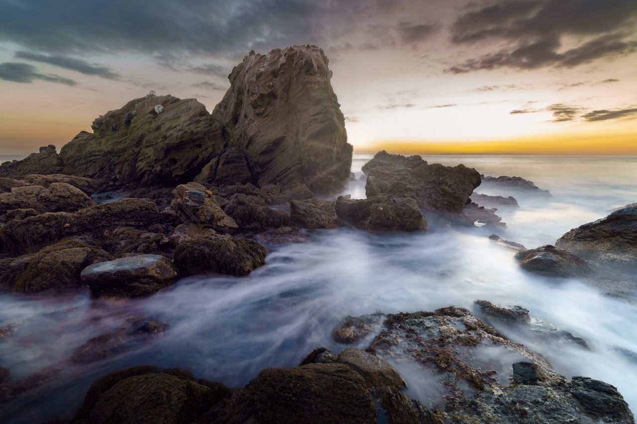 Dramatic seascape of rocky coastline during stormy sunset with crashing waves.