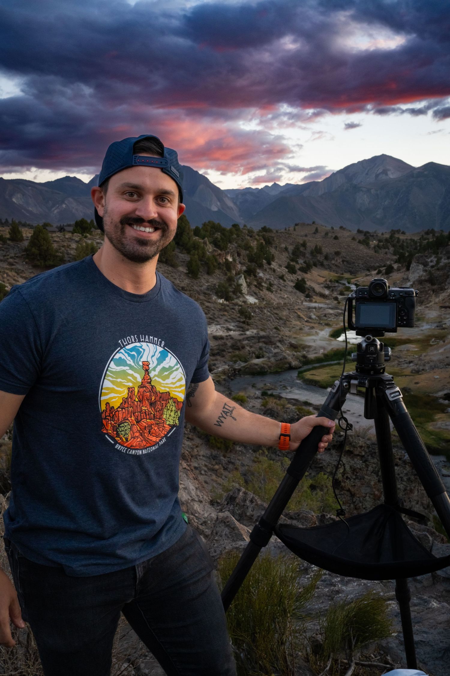 Photographer with camera equipment capturing sunset landscapes in a mountainous desert setting.