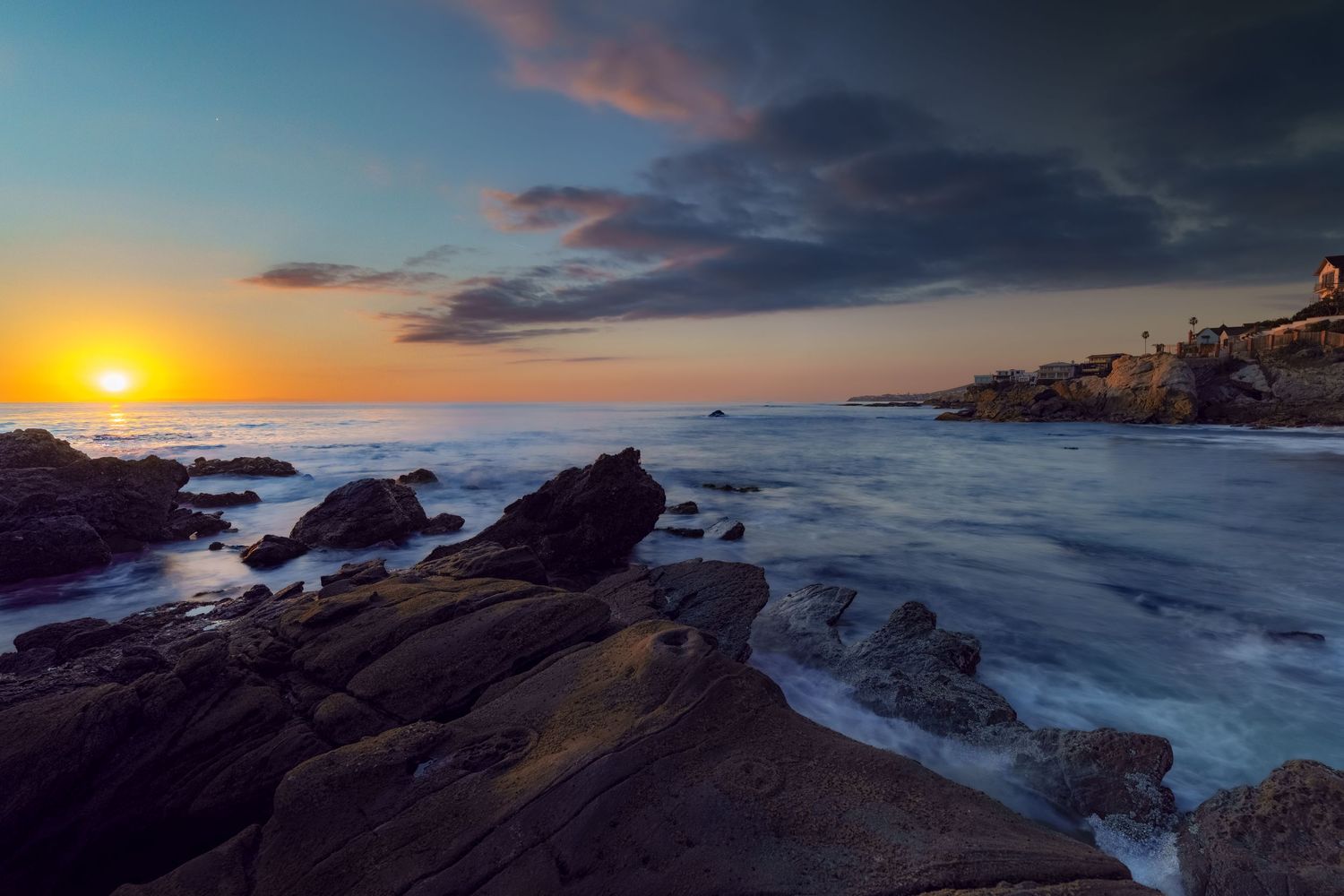 Cinematic landscape photograph of a dramatic sunset over the rocky cliffs and crashing waves of Laguna Beach California by Vince Shewmaker.