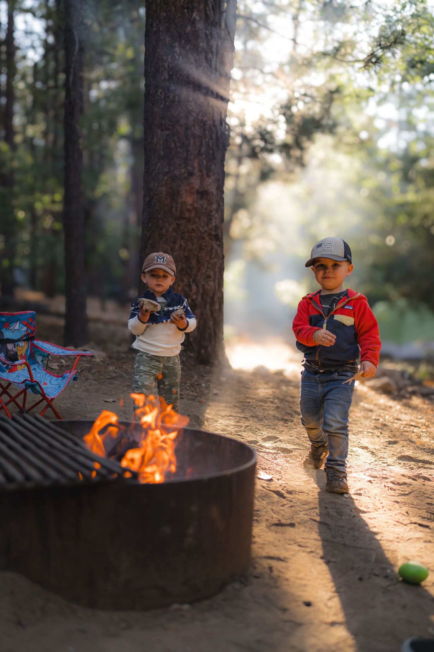 Campfire scene in forest with camping chairs and glowing flames.
