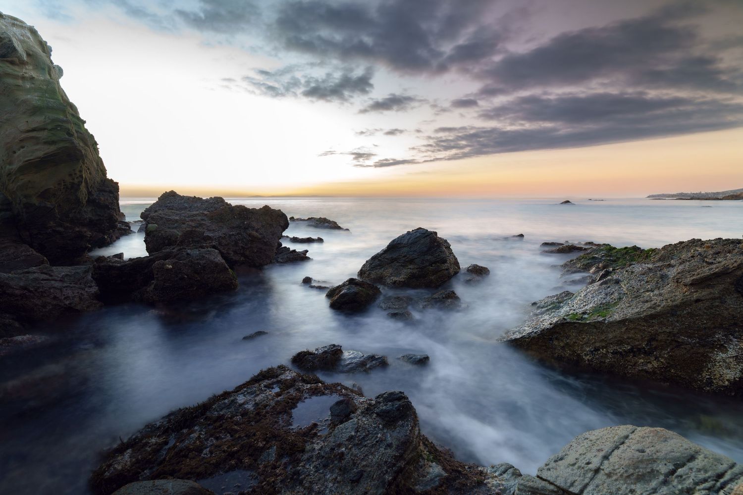 Cinematic landscape photograph of a dramatic sunset over the rocky cliffs and crashing waves of Laguna Beach California by Vince Shewmaker.