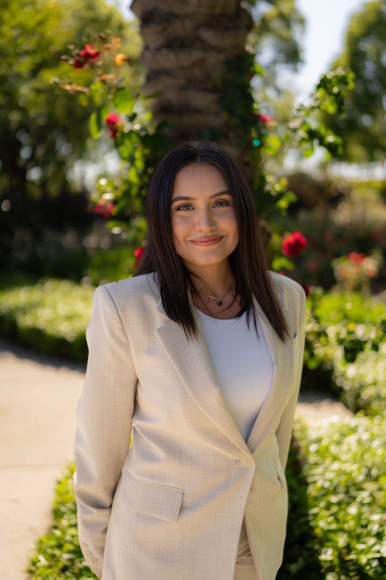 Portrait series of person in white blazer posing in garden with blooming flowers.