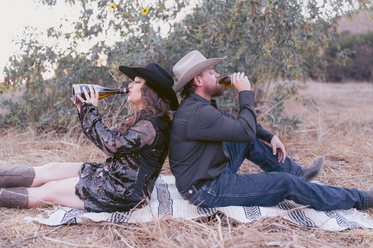 A couple laying together on blankets in a rustic outdoor setting during golden hour.