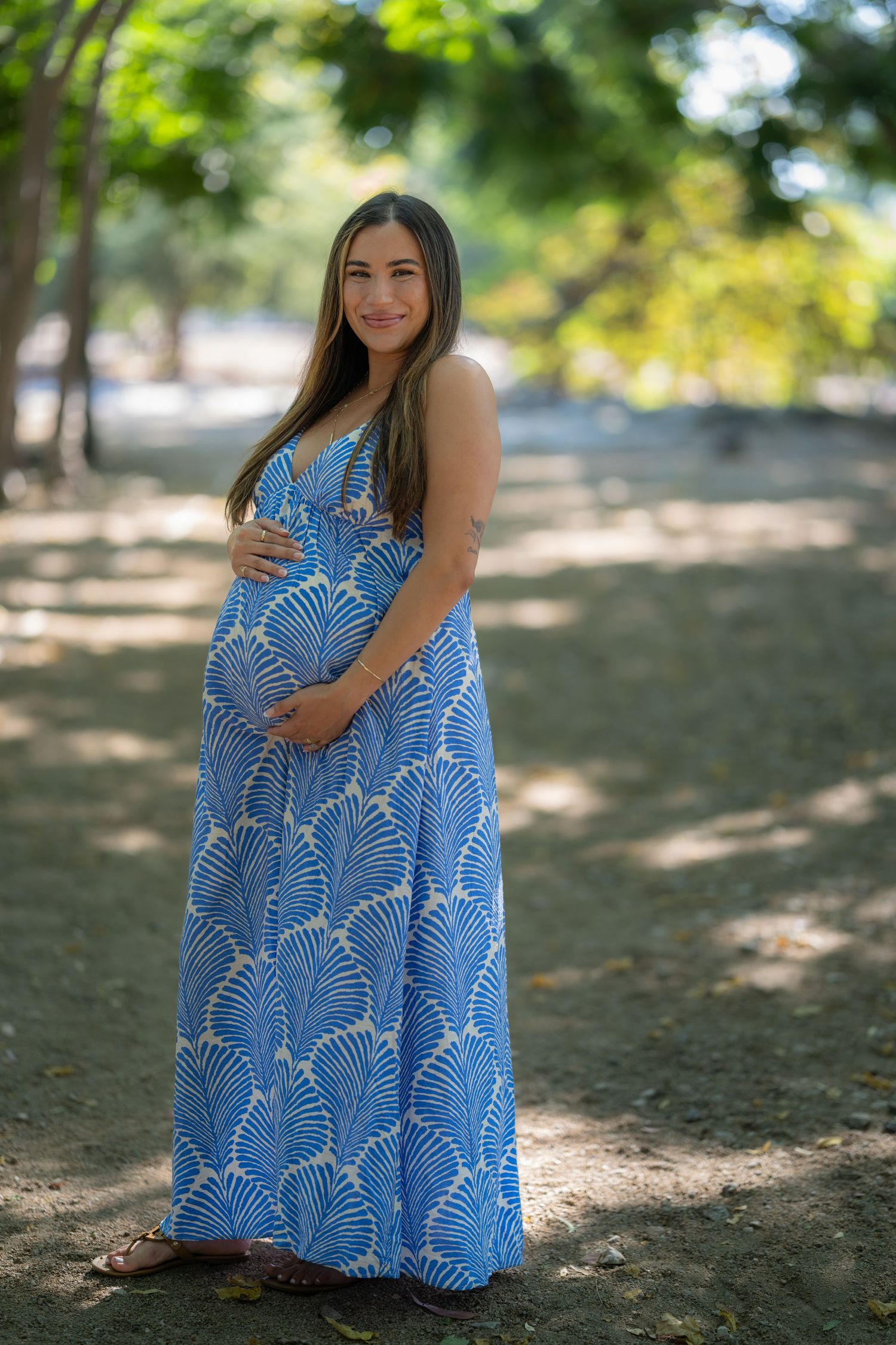 Cinematic golden hour portrait of a pregnant woman standing in tall grass on a rolling hill at sunset by Vince Shewmaker.