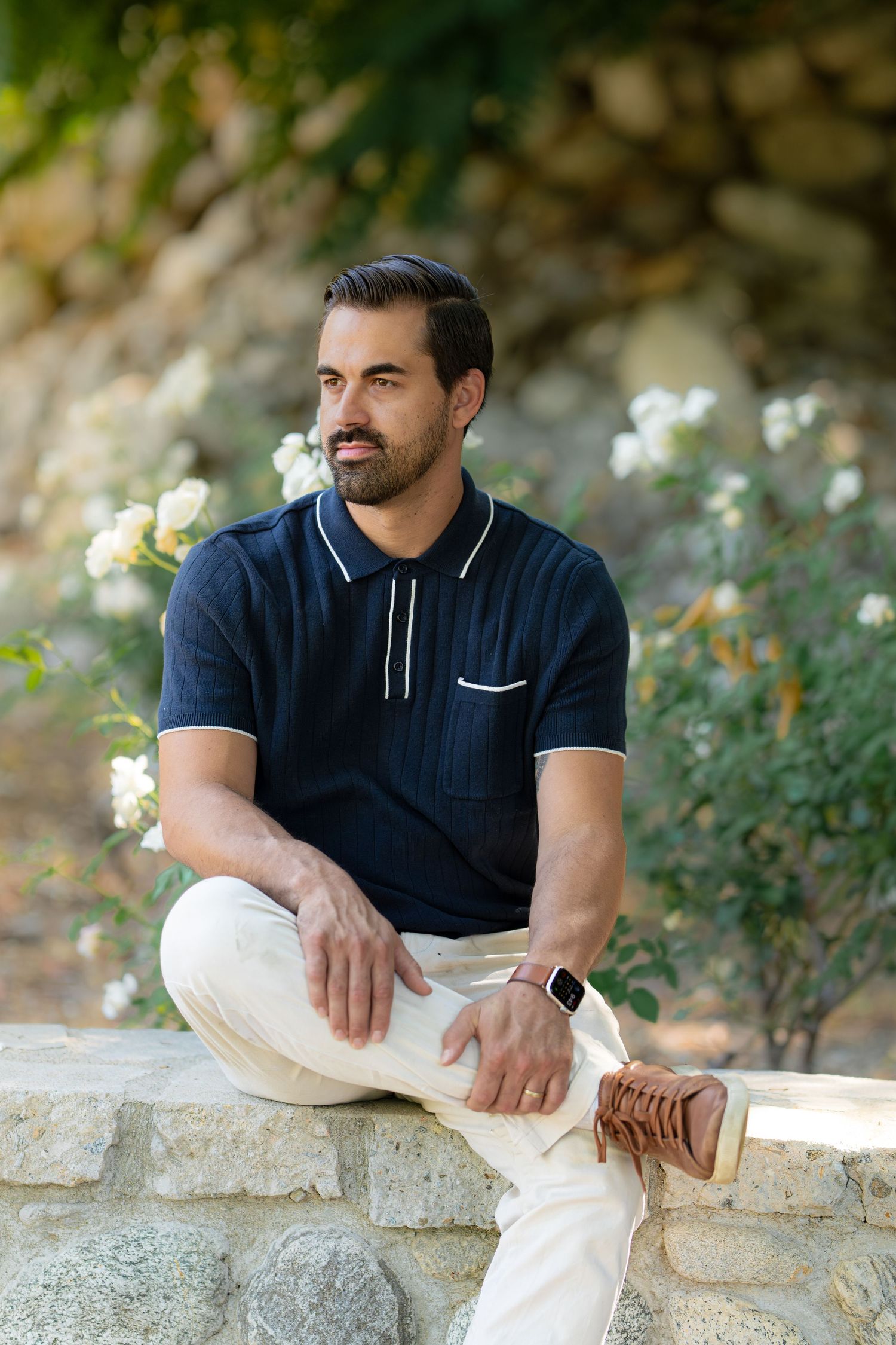 Casual outdoor portrait session featuring white pants and navy polo against a natural stone backdrop.