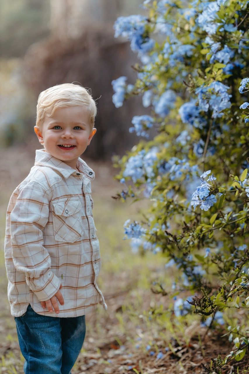 Young child in plaid shirt smiling and playing outdoors among autumn foliage.