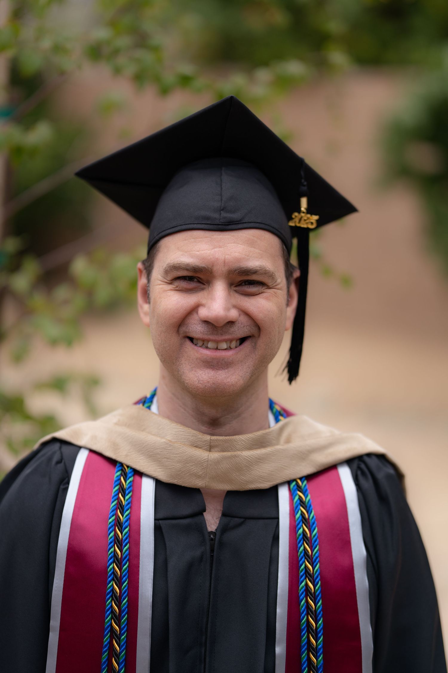 Graduate wearing traditional cap and gown with decorative stole shown in outdoor portrait sequence.