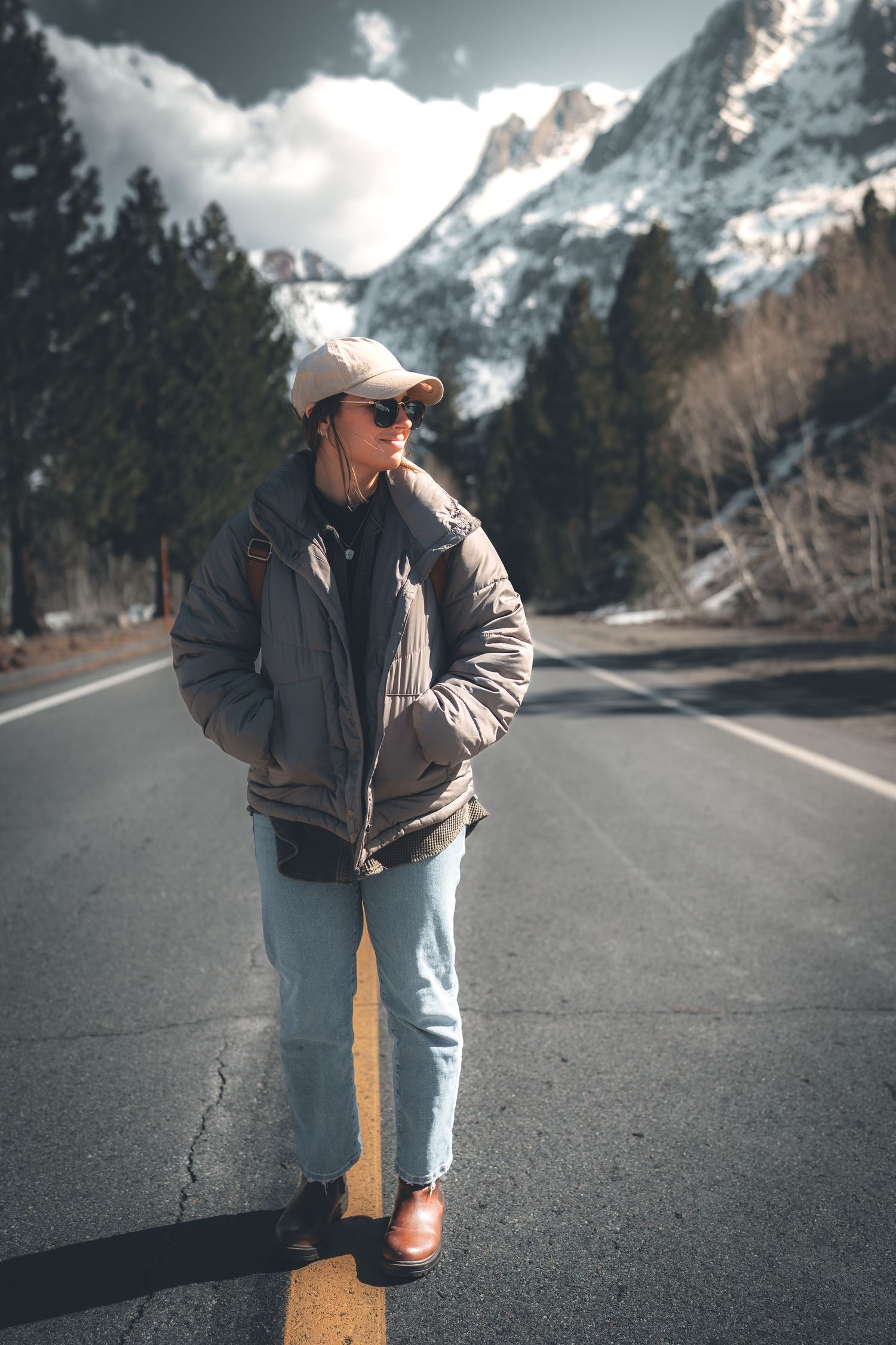 Winter scene with figure standing on empty mountain road surrounded by snowy peaks.