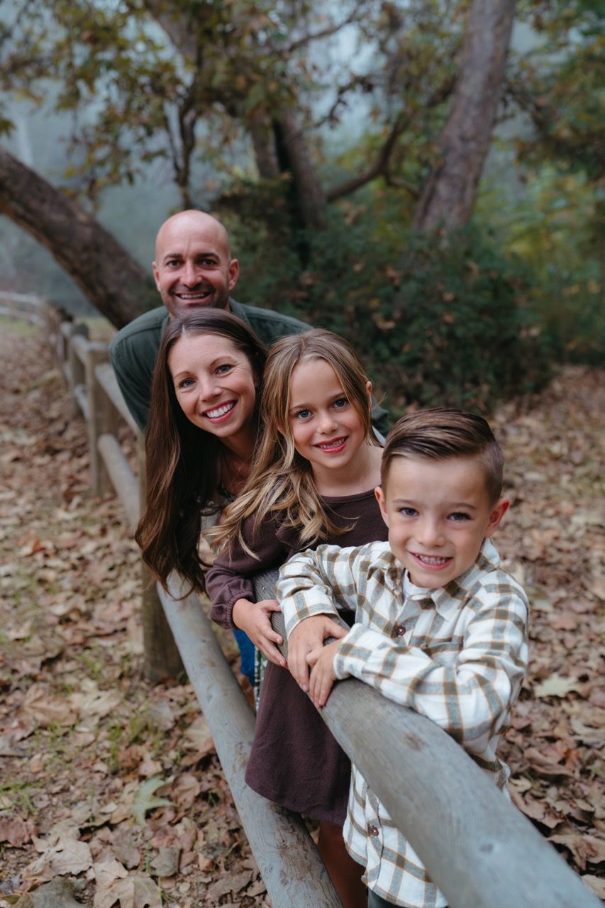 Family group poses playfully together on fallen autumn leaves in a wooded setting.