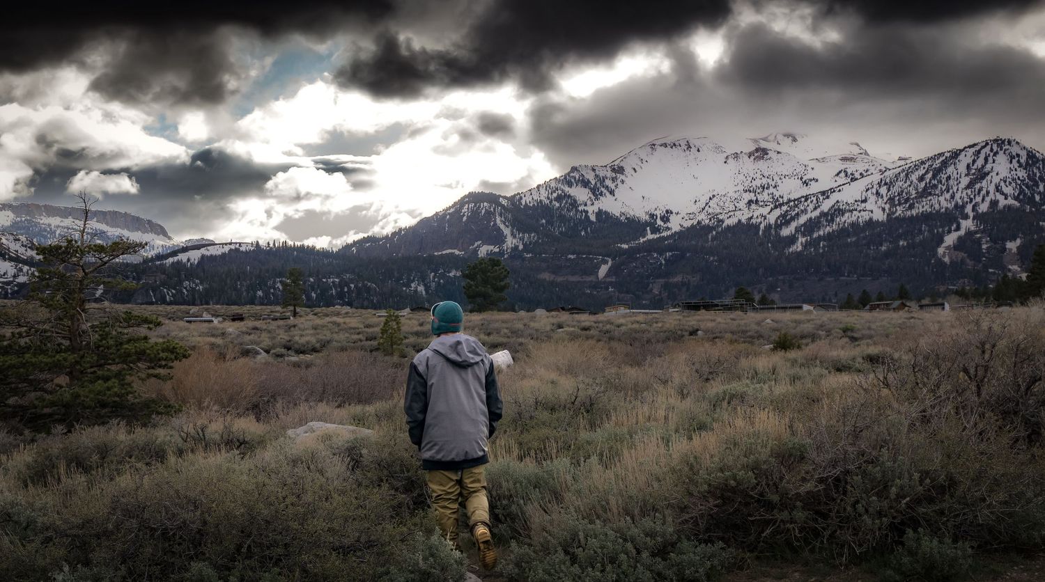 Dramatic storm clouds gather over snow-capped mountain peaks in a moody panoramic vista.