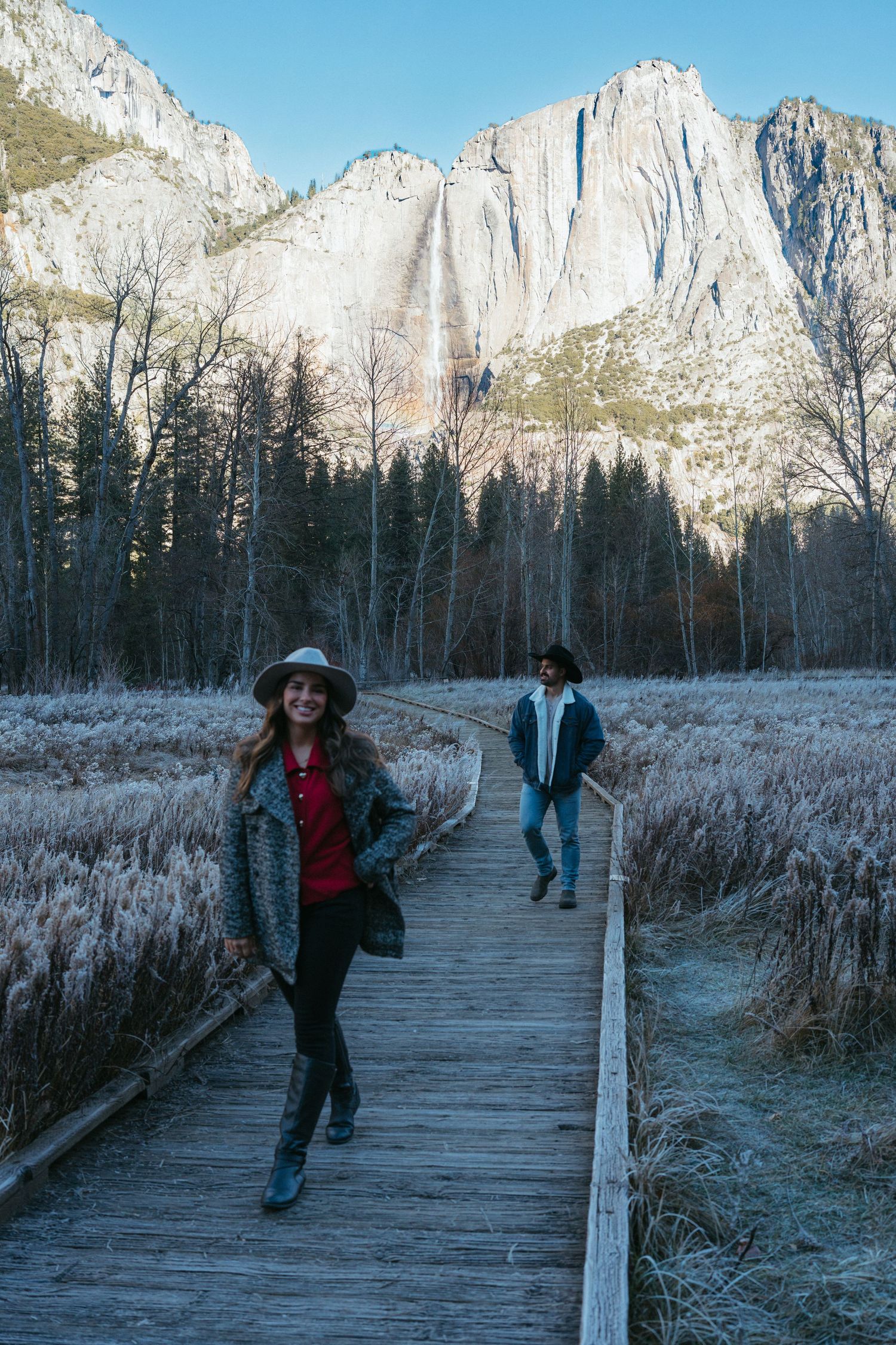 Wooden boardwalk trail through a frosty meadow with Yosemite's iconic granite cliffs in the background.