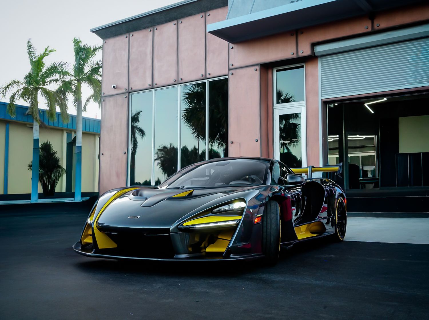 McLaren Senna. Black with Yellow detail trim on blacktop road in front of building.