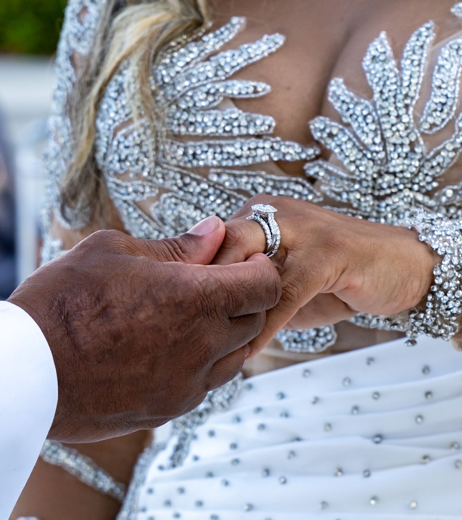 Close up of groom's hand taking bride's hand. Bride's dress is in background bedazzled.