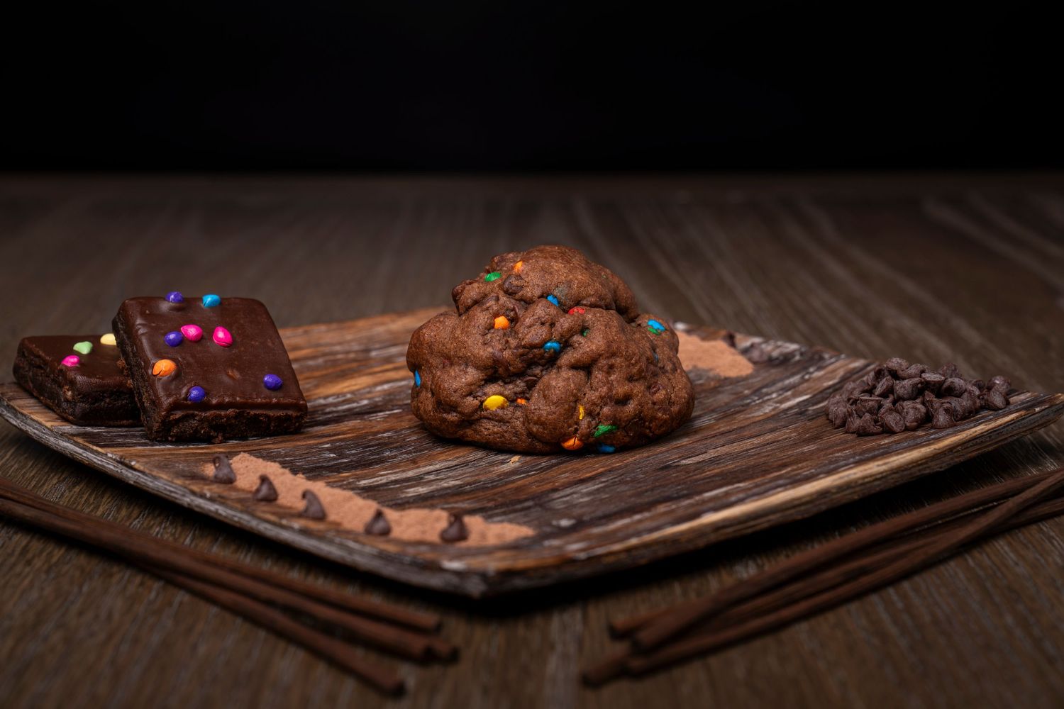 Food photography. Cookies and brownies a wooden table on a square wooden plate with chocolate chips, sprinkles, and cocoa powder