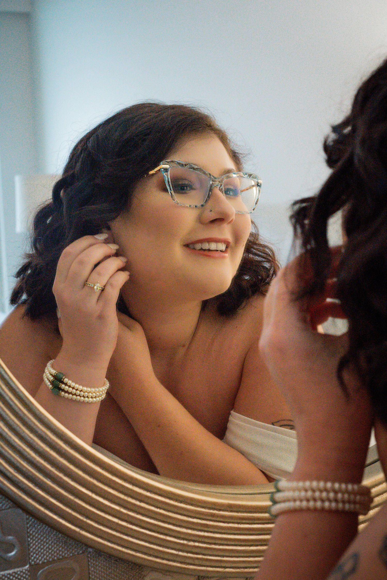 bride looking and smiling in mirror as she adjusts her earing.
