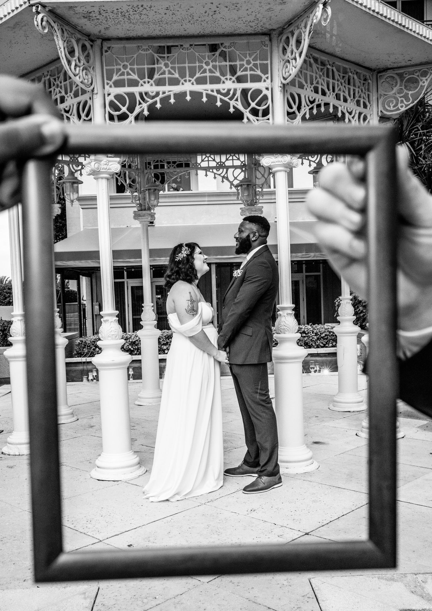 Black and white photo of husband and wife wedding photo. friends hold picture frame with man and woman holding hands in frame space.