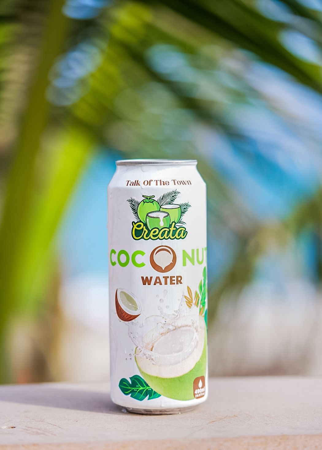 coconut water tall can sitting on ledge with tropical blurred greenery and skies in background.