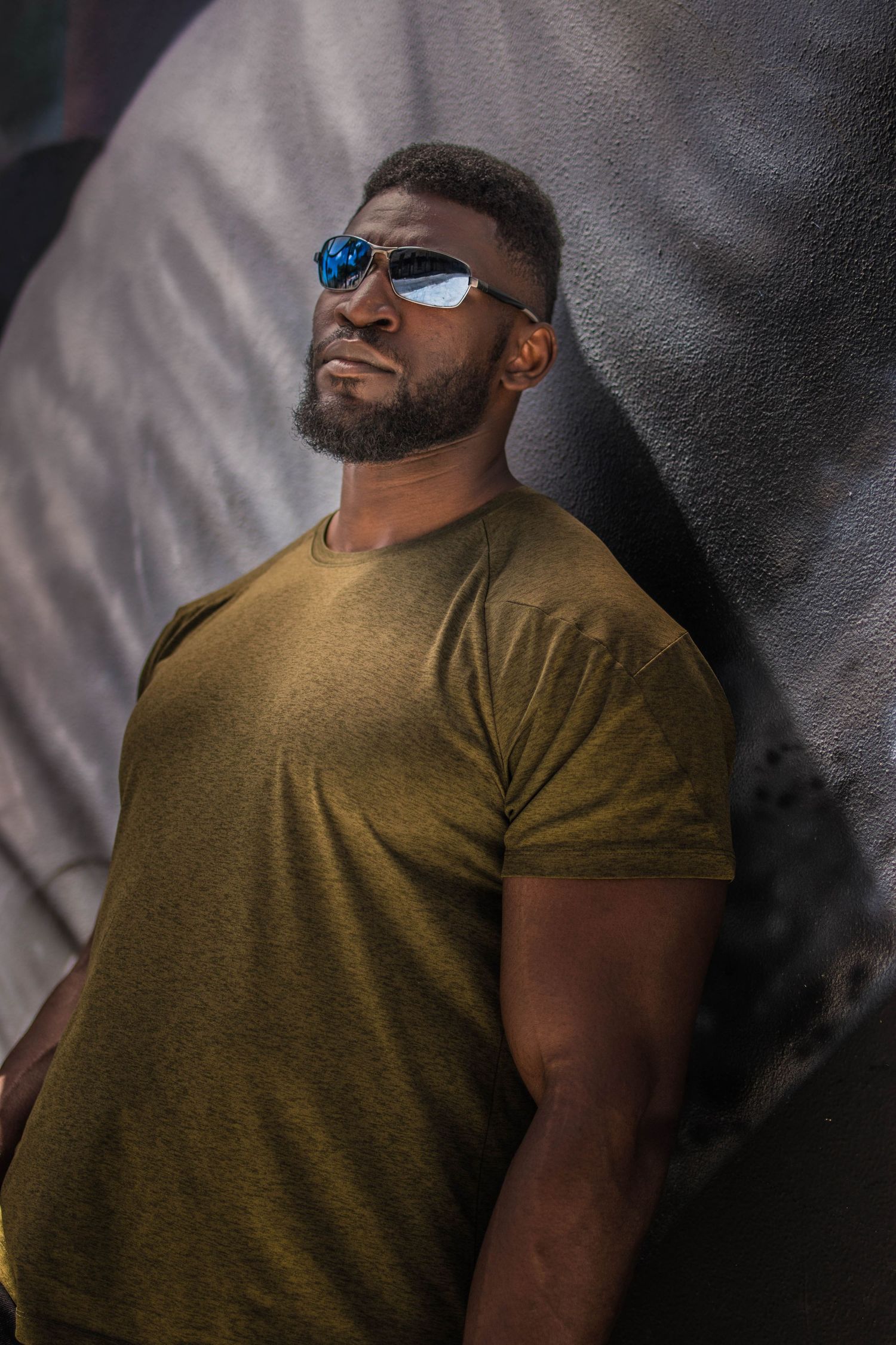 buff black man in sunglasses and green shirt posing up against mural background. moody edit