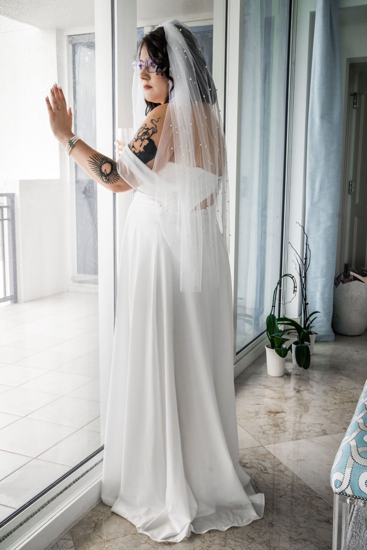 bride portrait hand up against window of hotel room. marble floors and blue drapery.