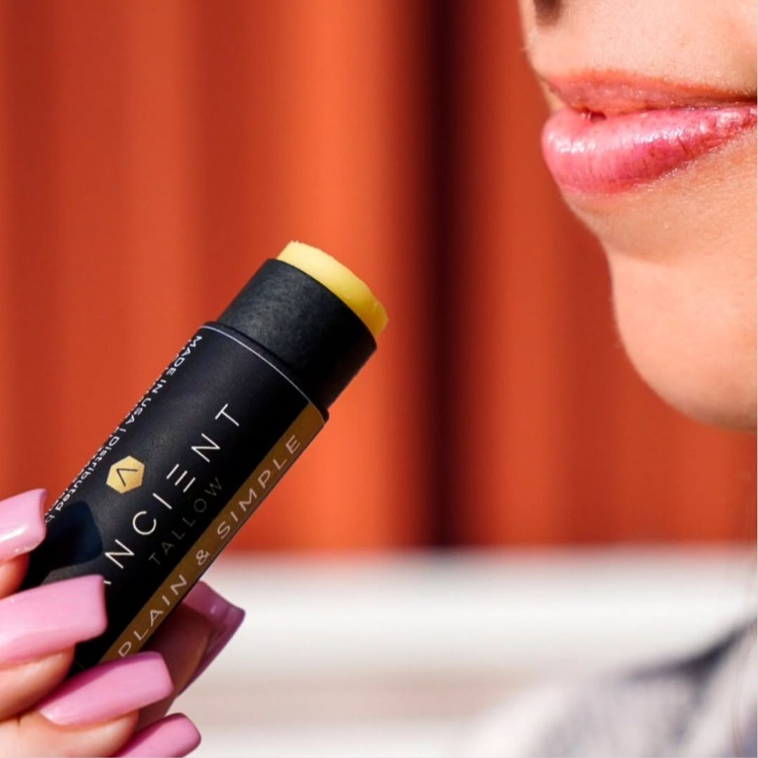 zoomed in on ancient tallow ChapStick or lip balm in hands of woman putting it up to her lips.