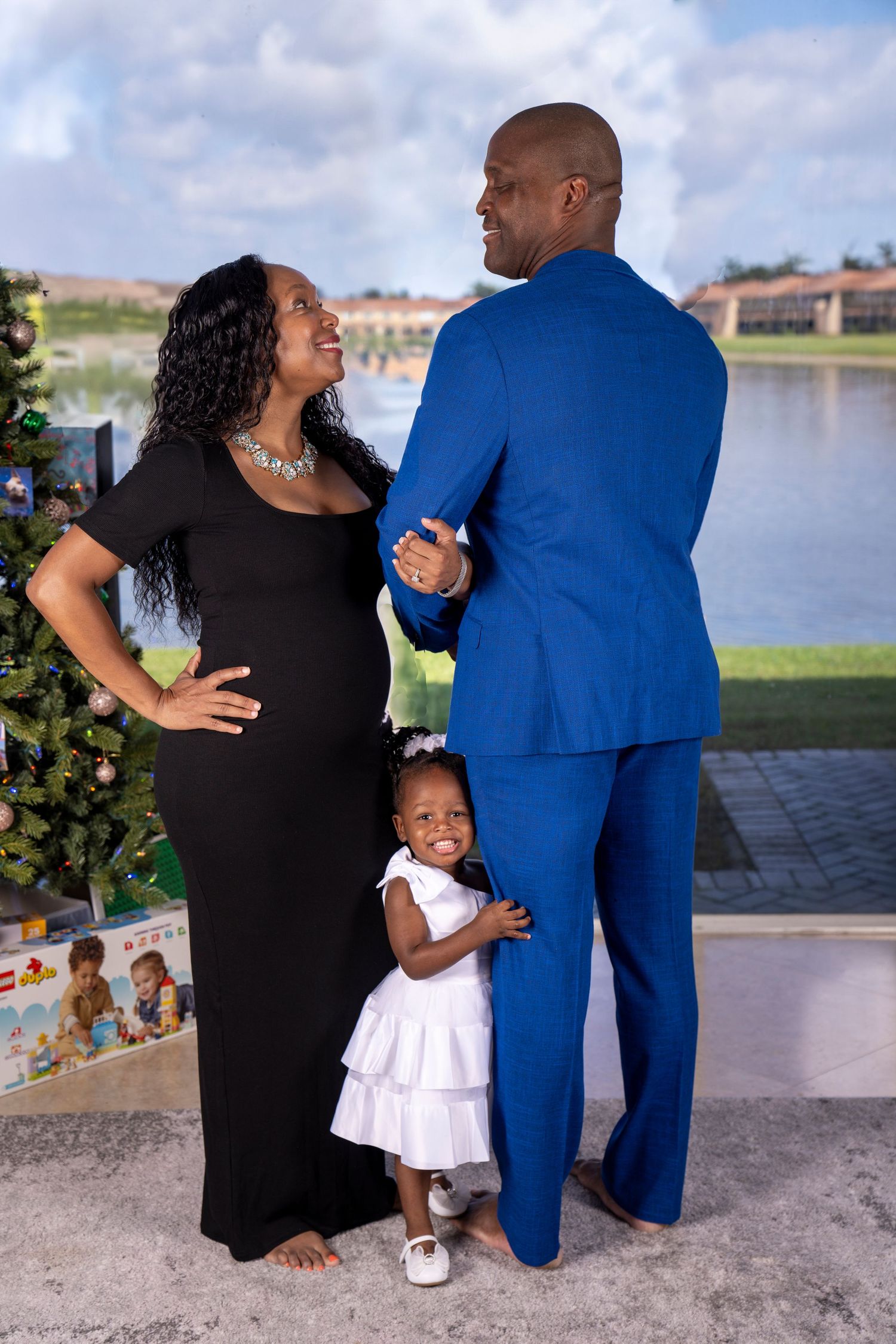 Husband faces away as mother holds his arm and gazes into each other's eyes while smiling. 2 year old holding father's leg smiling