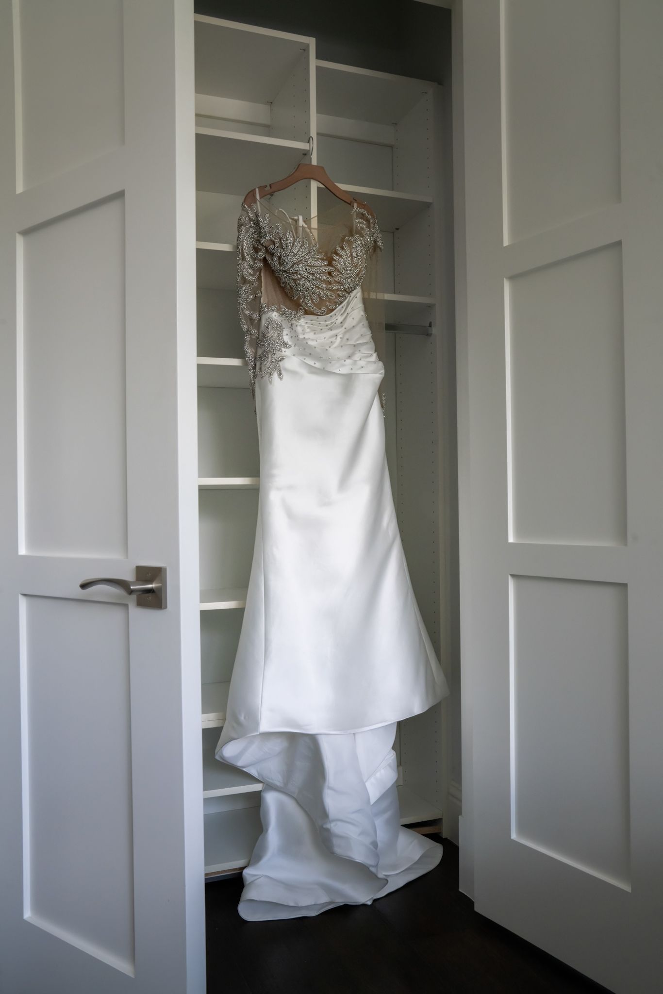 Wedding dress displayed hanging in closet with doors open to reveal dress.