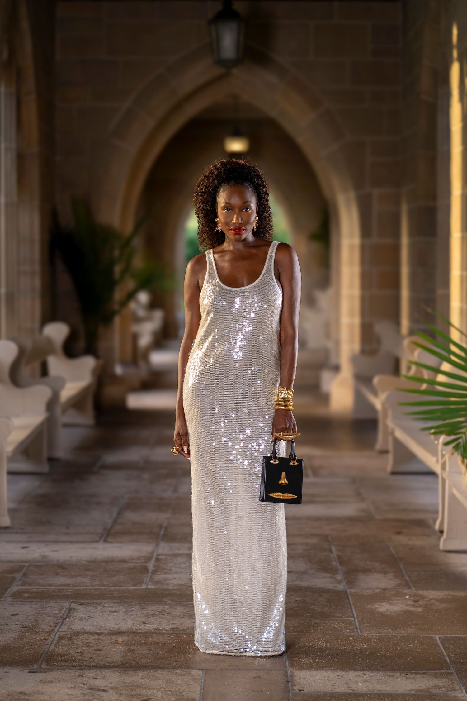 Modeling portrait of woman in Luxury white dress with sparkles holding upscale handbag in long corridor and archway.