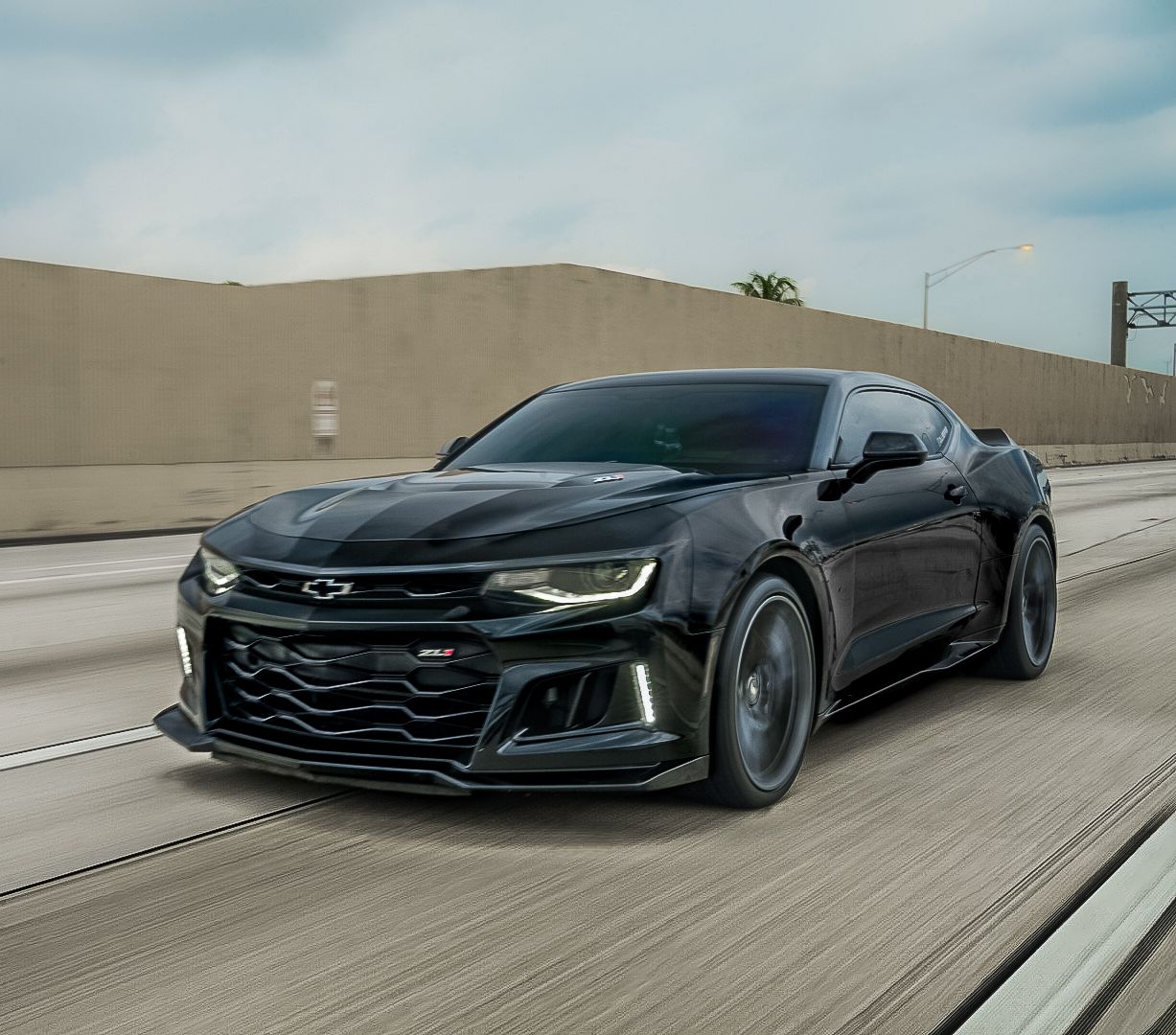 Black Camaro ZL1 on highway. Photo is a rolling shot with ground blurred and car in focus.