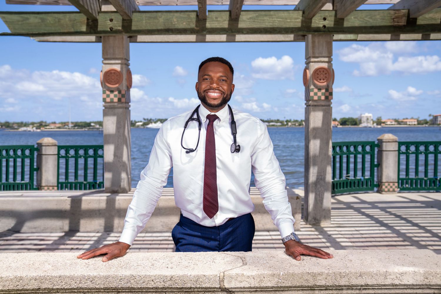 Doctor posing in Palm beach architecture and canopy with blue skies blurred in background. stethoscope on neck.