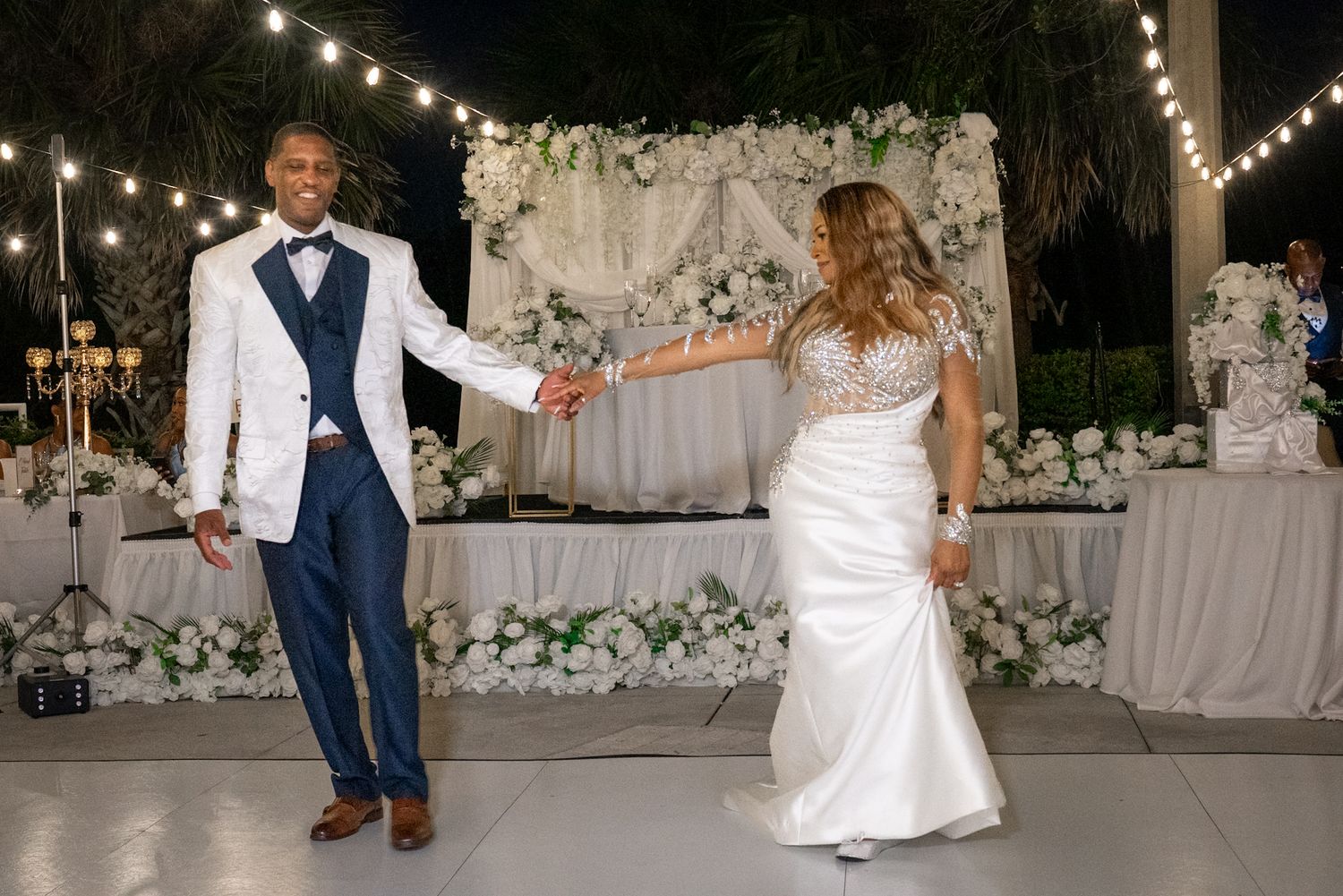 bride and groom dancing on dancefloor on outside patio lined with lights and flowers.