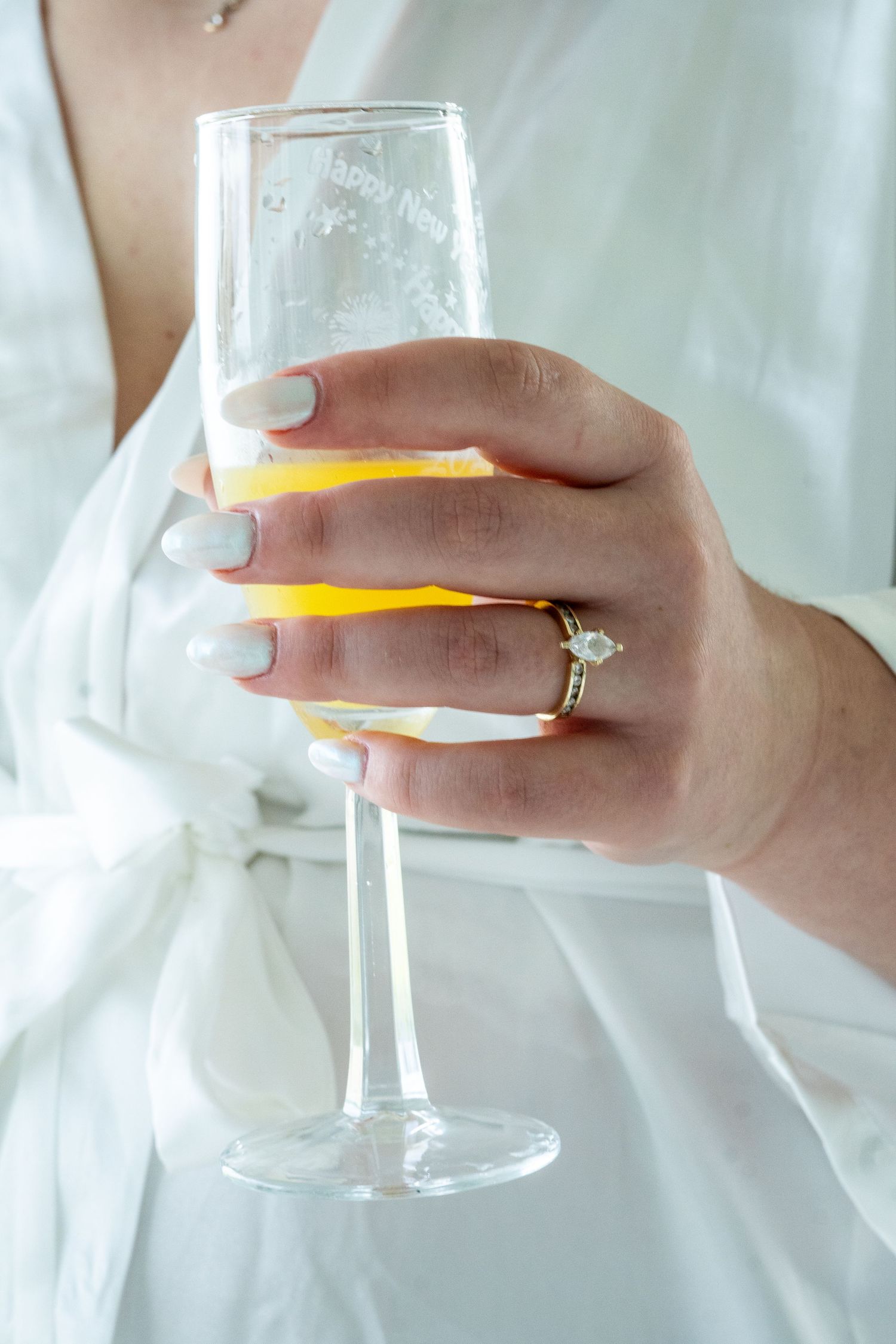 close up of bride's hands in white robe. in her hands is a mimosa and close up of ring and nails.