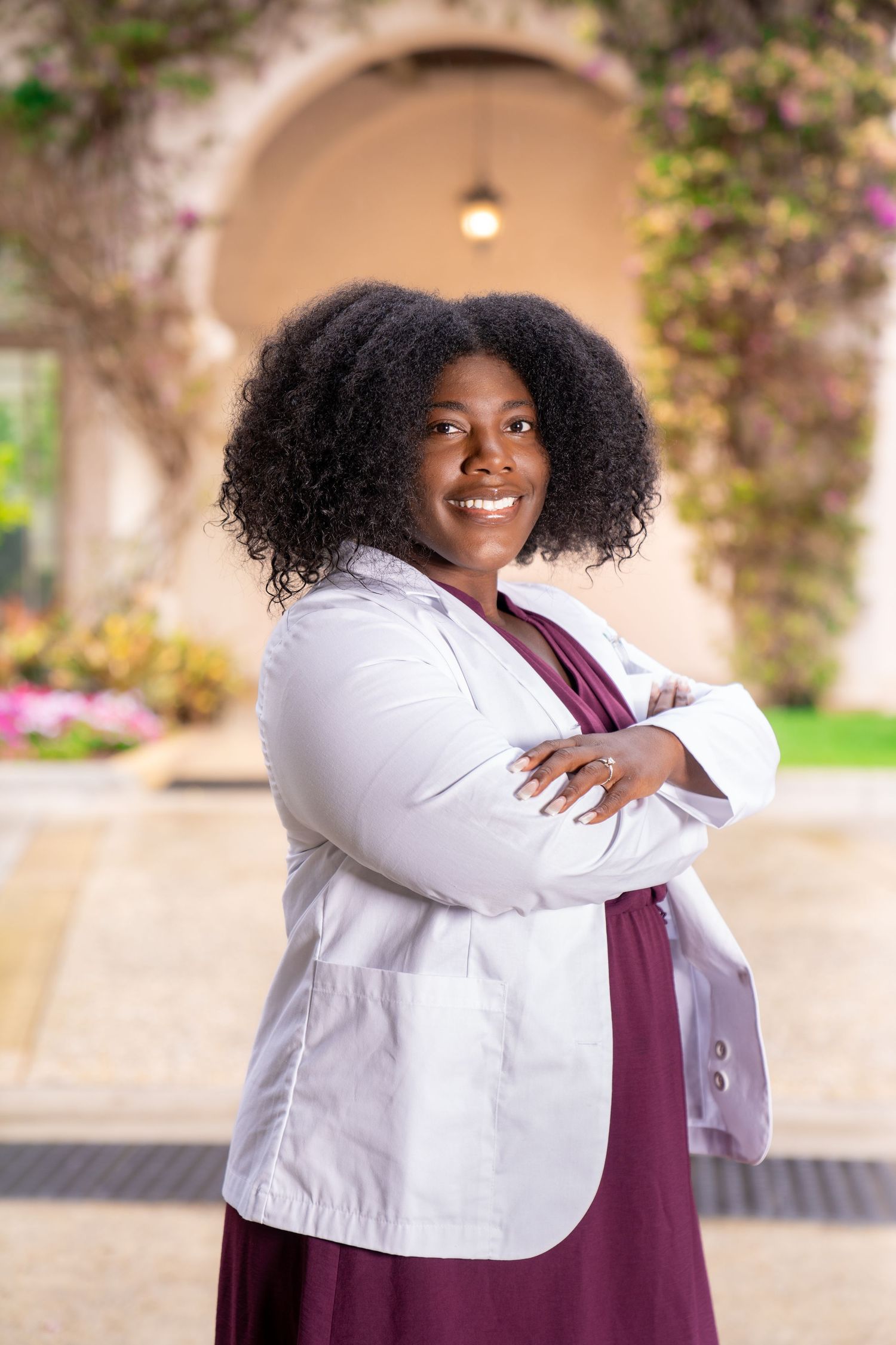 black Doctor headshot posing in front of Worth Avenue street with greenery, flowery, archways in blur in background.