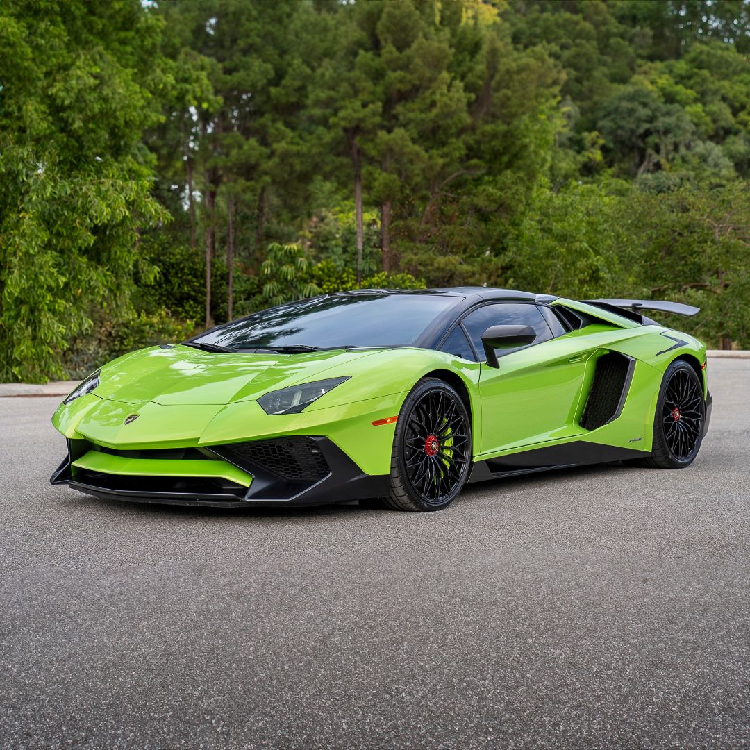 Green Lamborghini Aventador automotive portrait on concrete with forest in background.