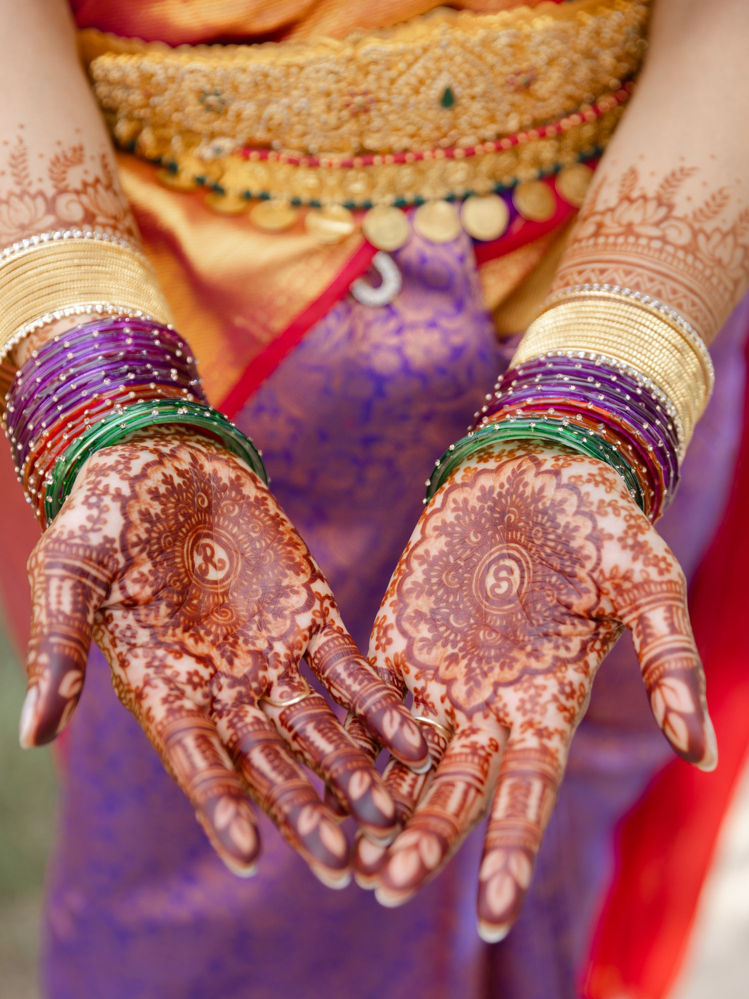 Indian bride displaying intricate henna mehndi designs on hands adorned with colorful bangles.