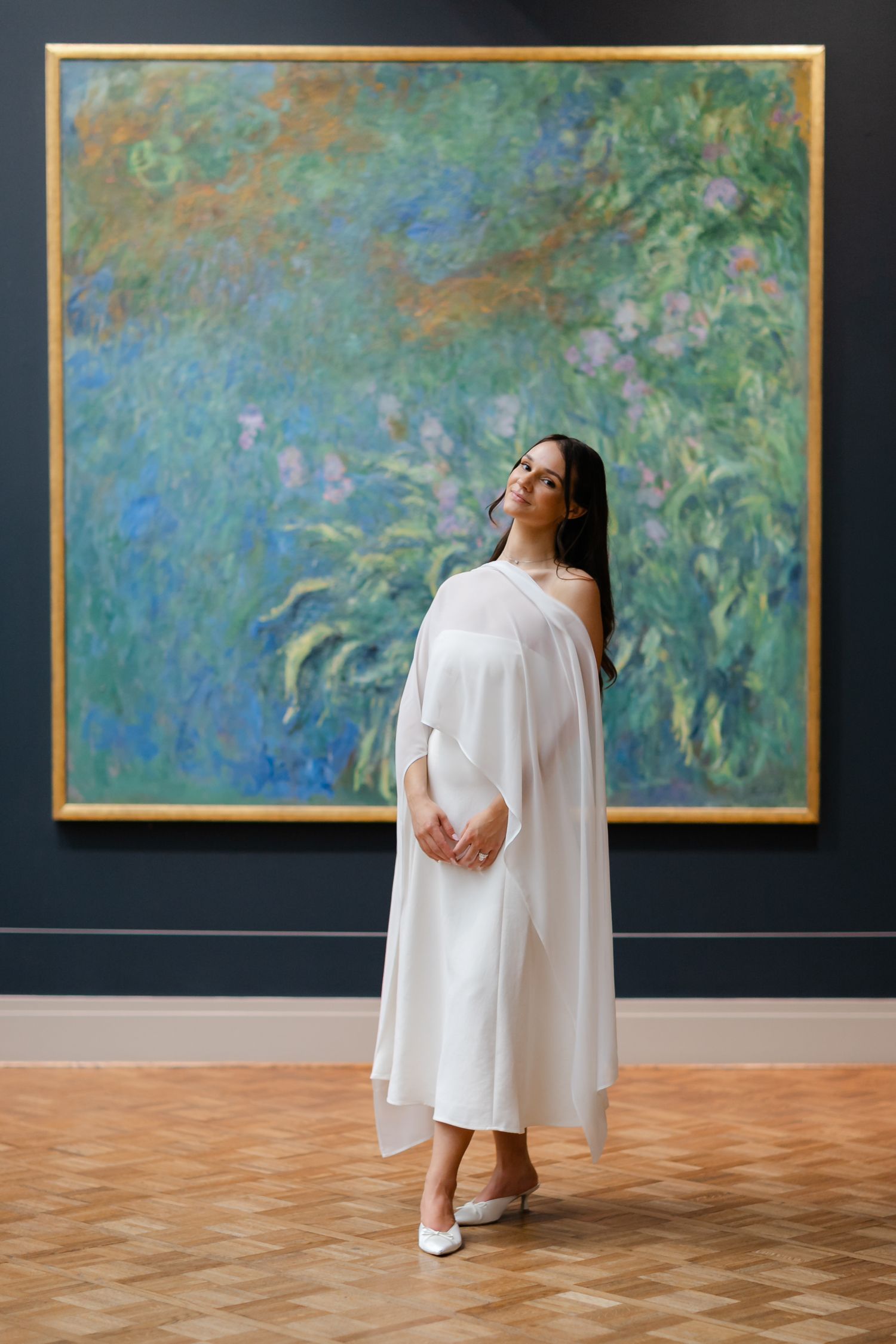 Woman in white dress standing before a large Monet impressionist painting in an art museum gallery.