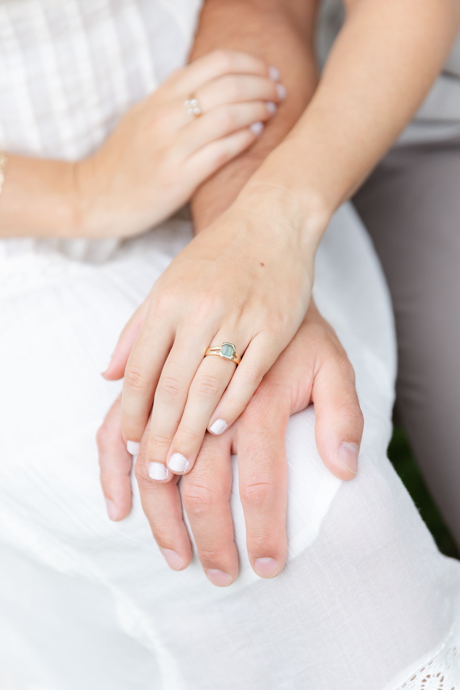 Close-up of two hands with white manicured nails, one wearing a delicate gold ring with a turquoise gemstone.