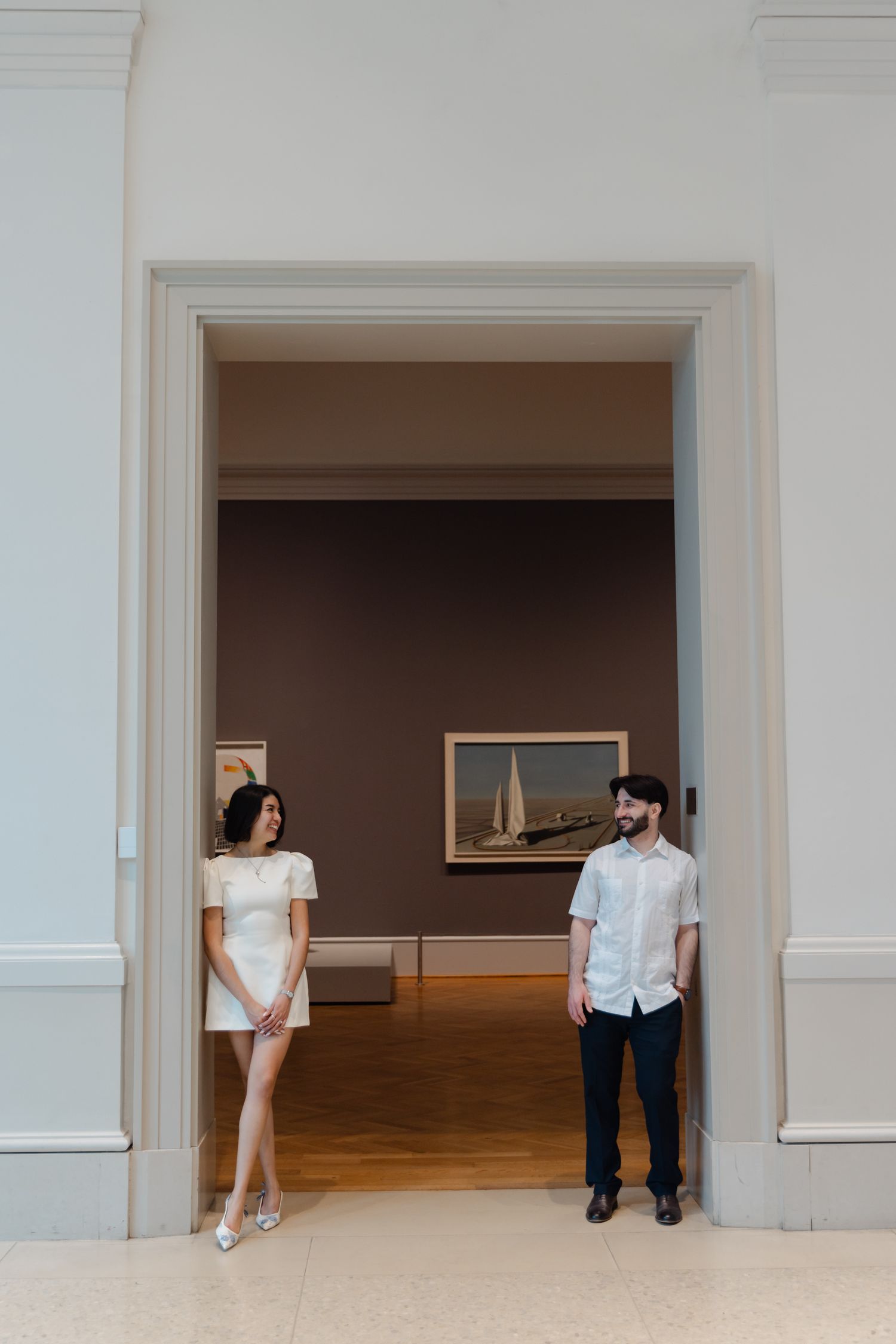 Couple standing in elegant museum doorway with artwork visible in background gallery beyond.