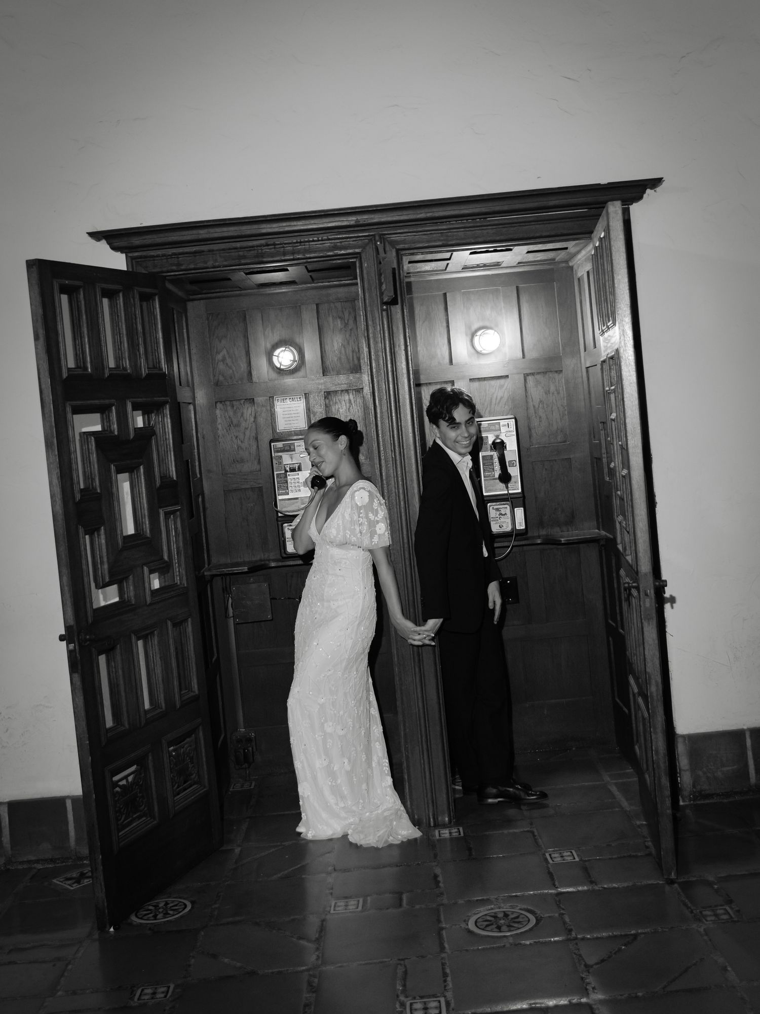 Black and white photo of a bride and groom holding hands in a doorway on their wedding day.