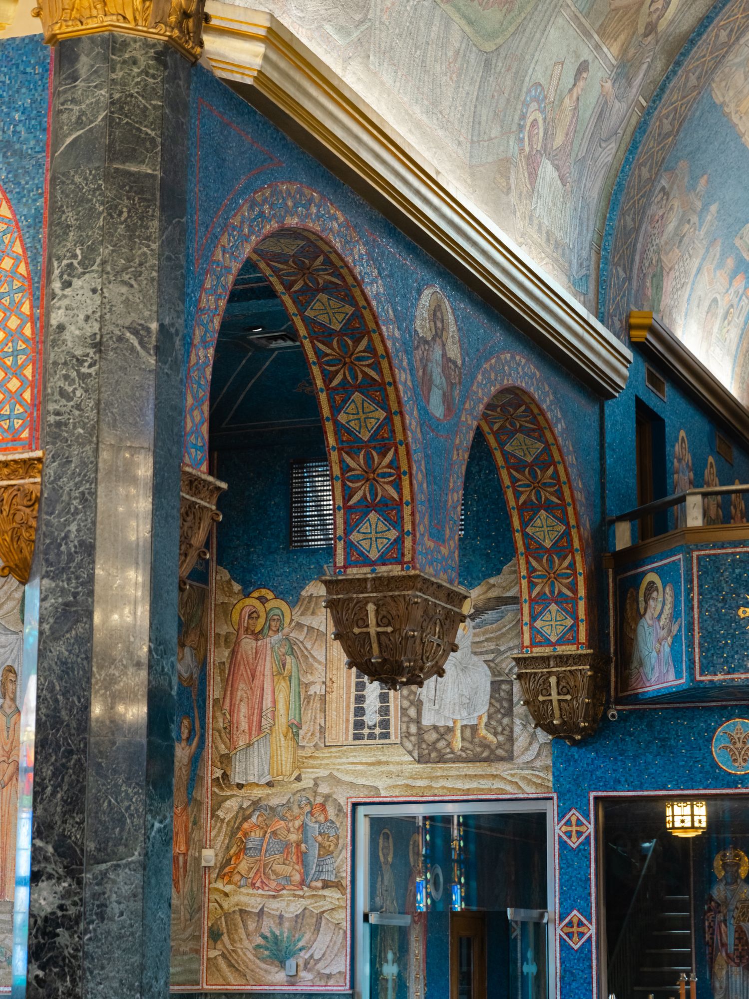 Byzantine church interior with ornate blue mosaic walls, decorative arches, religious frescoes, and gold accents.