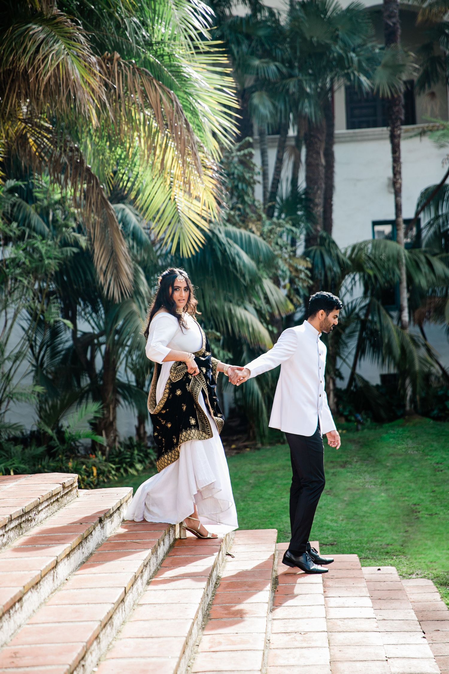 Couple walking down outdoor stone steps surrounded by palm trees.