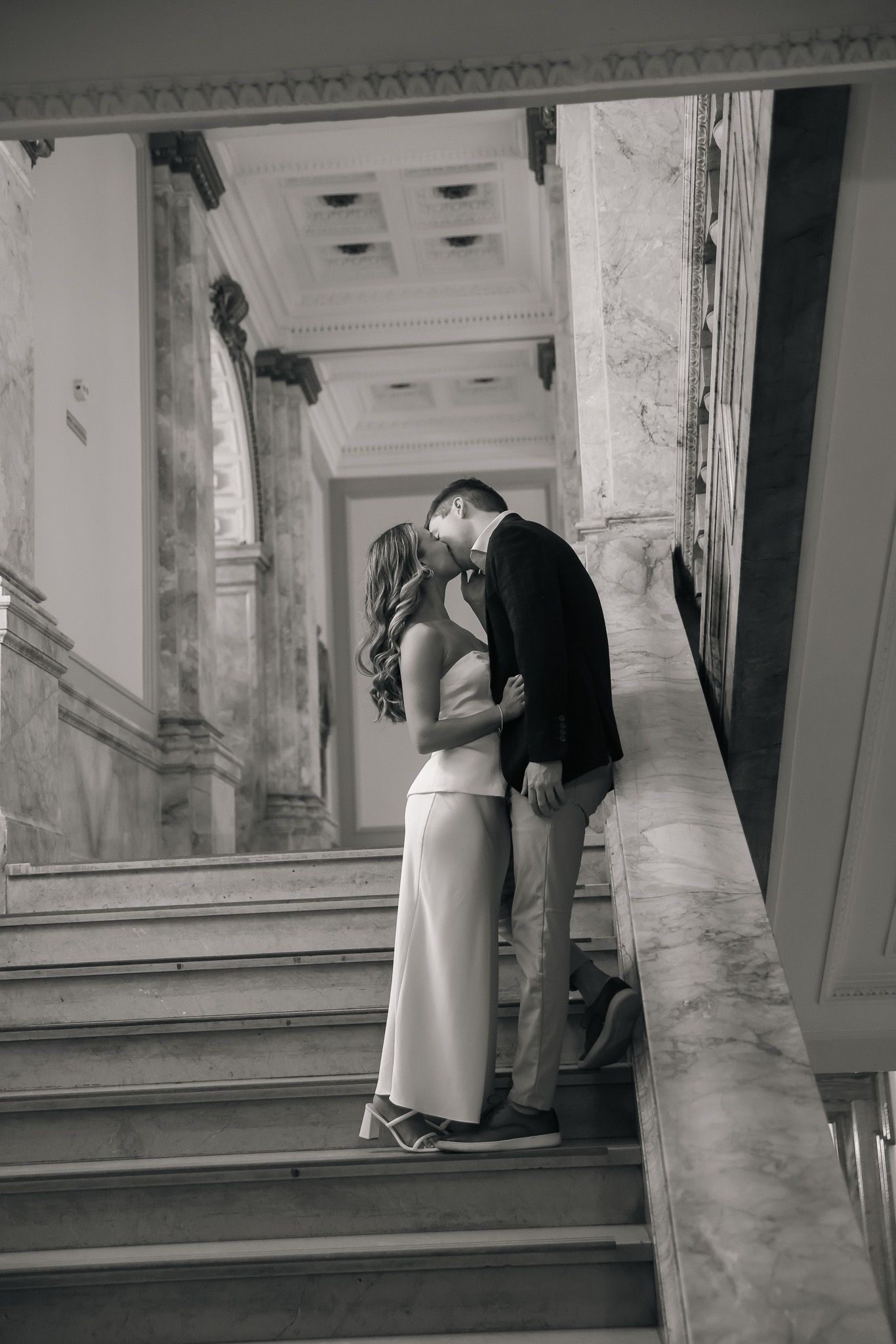 A romantic black and white photo sequence showing a couple kissing on elegant marble stairs in a classic building.