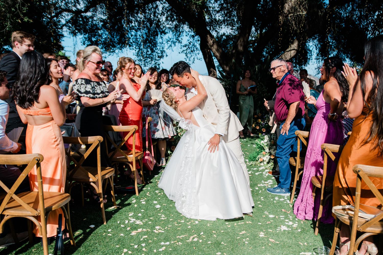 Wedding celebration with guests cheering as couple shares a romantic moment on grass.