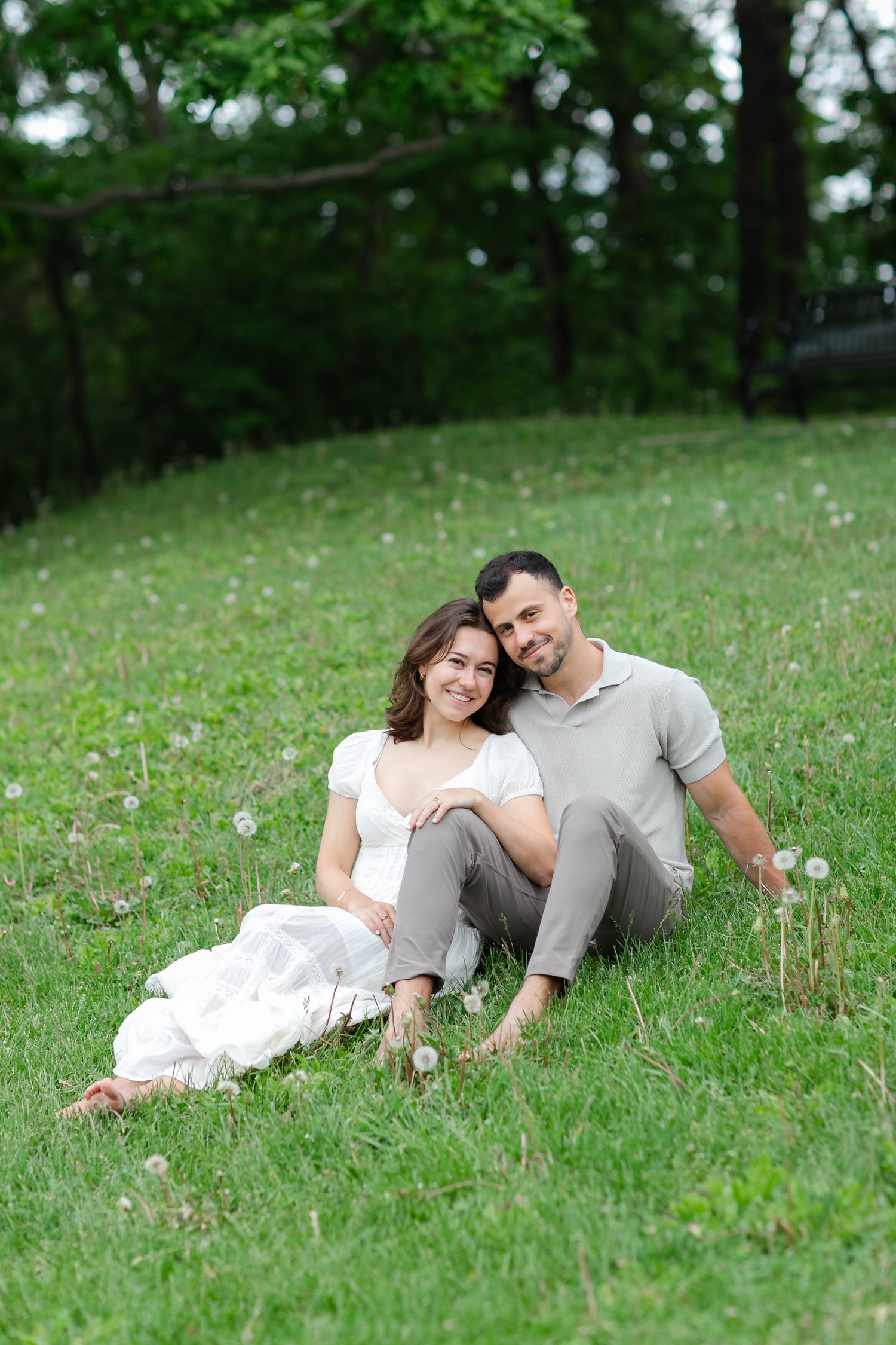 Happy couple sitting together on lush green grass in a park, smiling and embracing on a summer day.