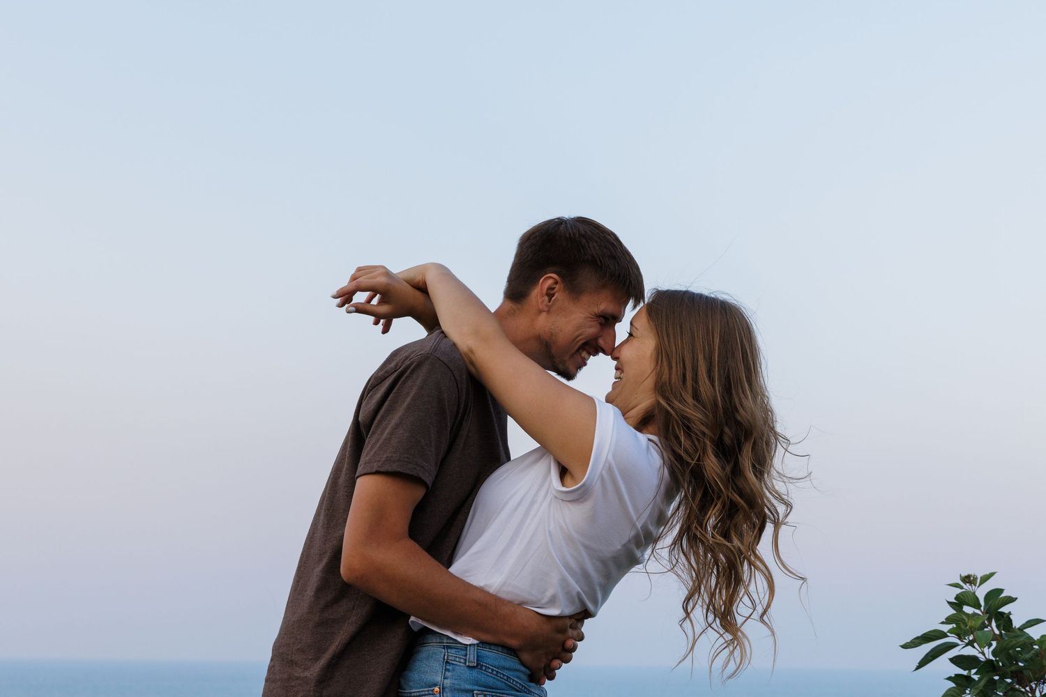 Romantic couple nearly kissing outdoors with a clear blue sky backdrop.
